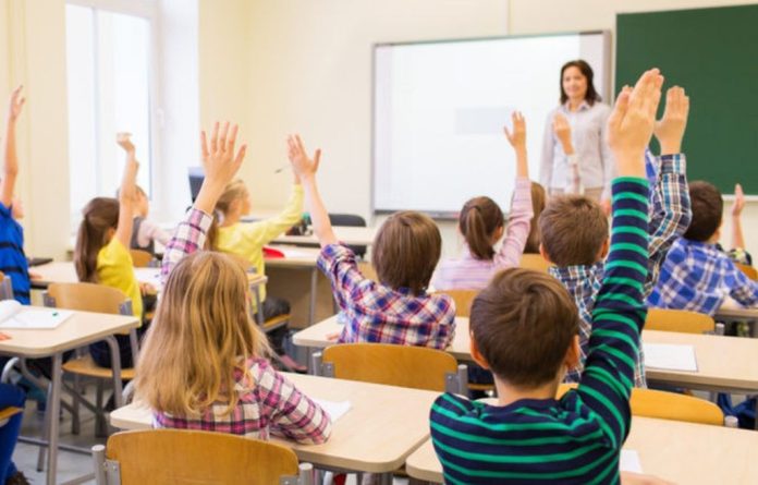 group of school kids raising hands in classroom